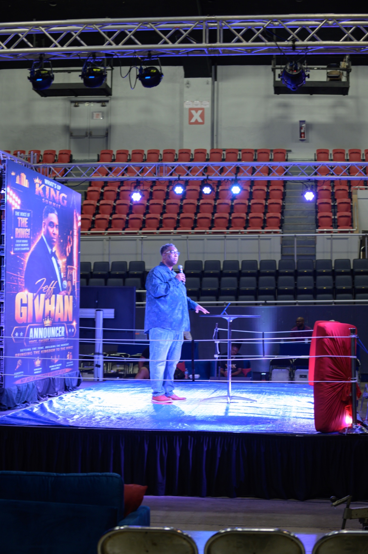 Jeff Givhan speaking from a clear lectern on the What's Up King stage