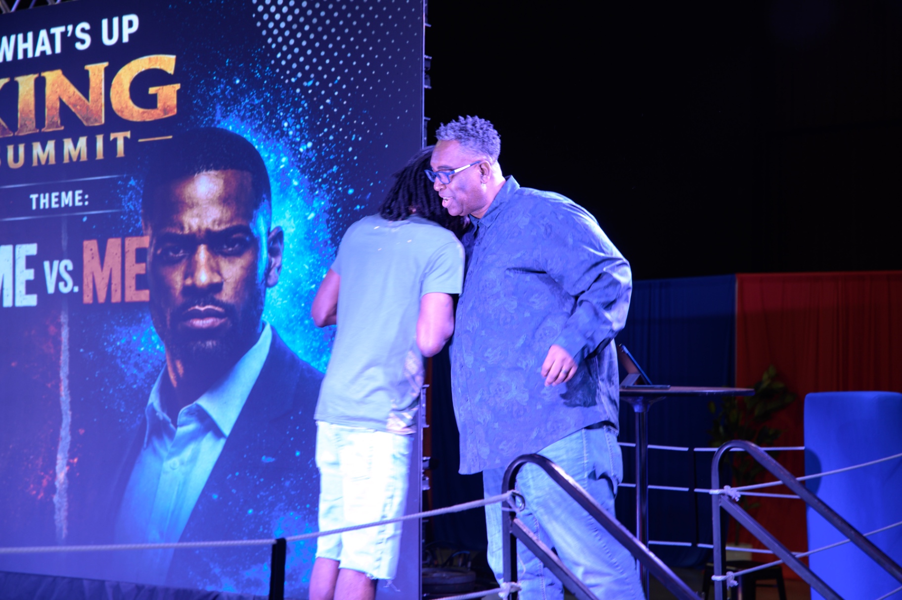 Two summit speakers greeting one another beside the Me vs. Me backdrop