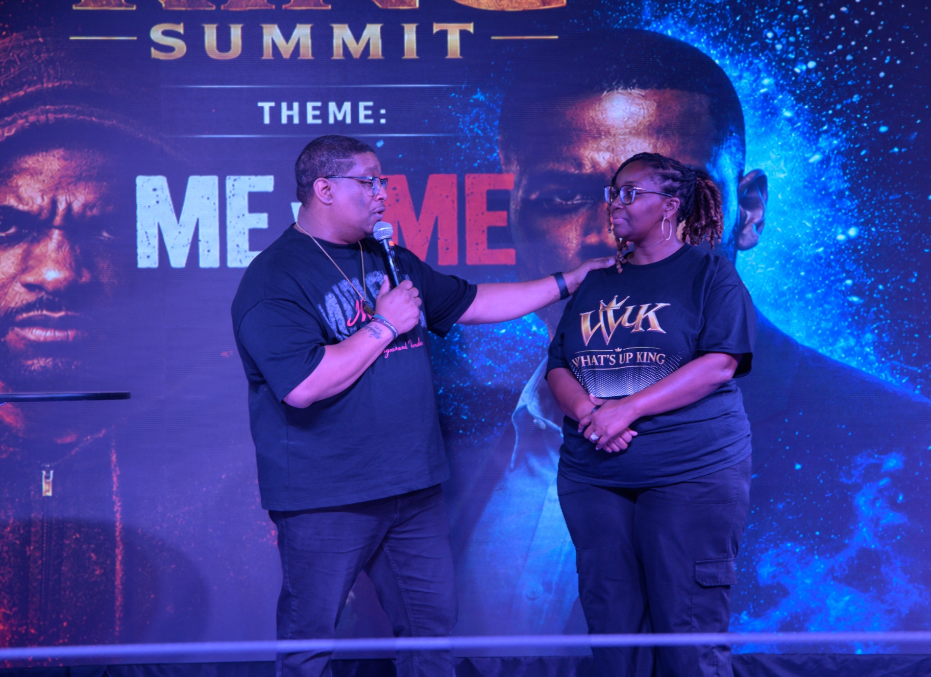 A speaker sharing a microphone with a woman wearing a What's Up King shirt